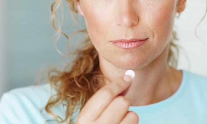 Portrait of a woman about to take some pain medication with a glass of water