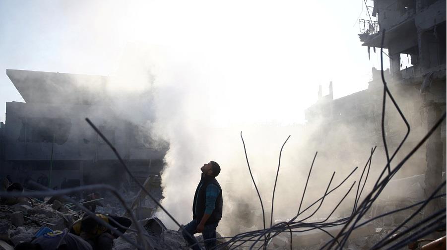 Man stands on rubble of damaged buildings after airstrike in Hamoria, Damascus