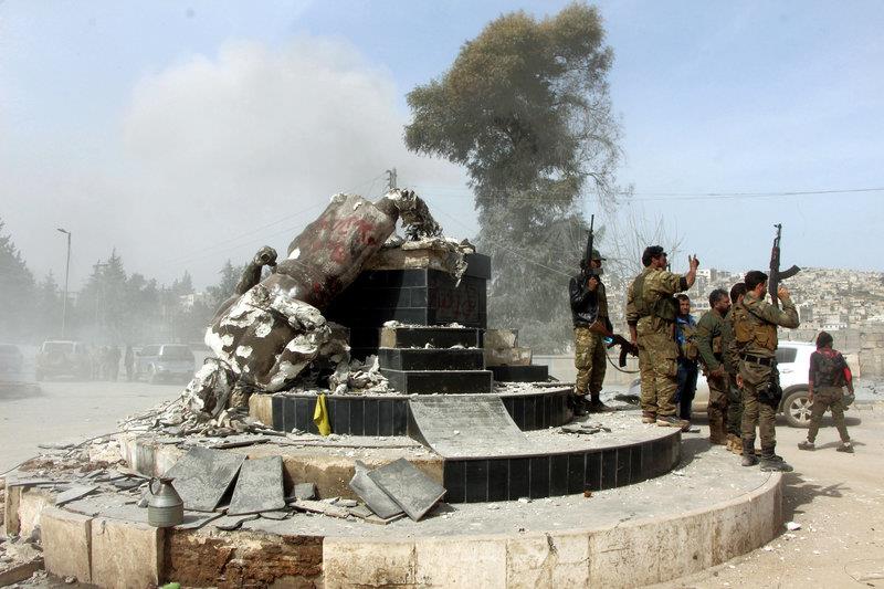 Turkey-backed Free Syrian Army soldiers celebrate around a statue of Kawa, a mythology figure in Kurdish culture, after they have destroyed it in the city center of Afrin, northwestern Syria, early Sunday, March 18, 2018. Turkey's President Recep Tayyip Erdogan said Sunday that allied Syrian forces have taken "total" control of the town center of Afrin, the target of a nearly two-month-old Turkish offensive against a Syrian Kurdish militia, which said fighting was still underway. Erdogan said the Turkish flag and the flag of the Syrian opposition fighters have been raised in the town, previously controlled by the Kurdish militia known as the People's Defense Units, or YPG. (Hasan K?rm?zitas/DHA-Depo Photos via AP)