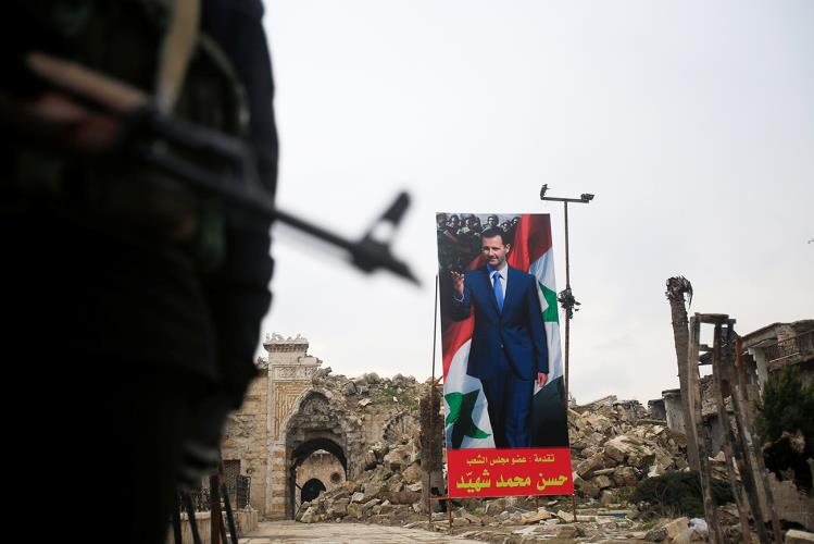 A Syrian army soldier stands guard as a poster depicting Syria's President Bashar al-Assad is seen in the background in the Old City of Aleppo
