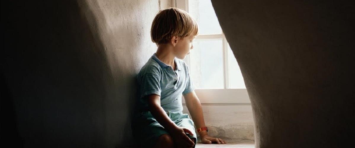 Boy (6-7) sitting on window sill, looking out window