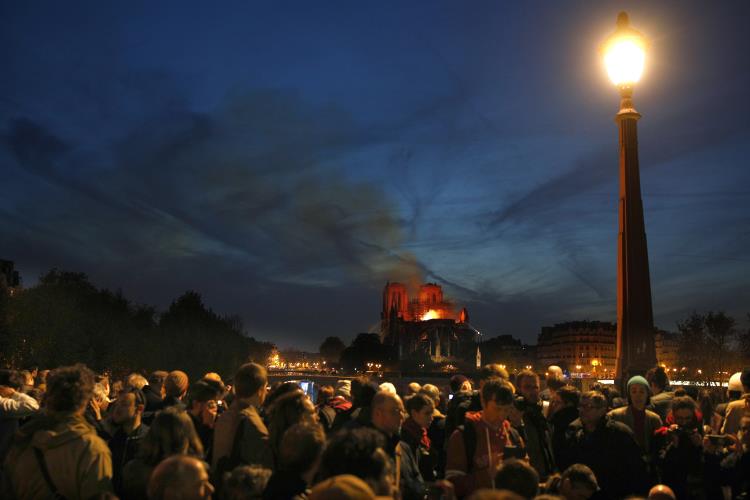 epa07508911 Parisians gather on the Seine river bank to look at the flames burning the roof of the Notre-Dame Cathedral in Paris, France, 15 April 2019. A fire started in the late afternoon in one of the most visited monuments of the French capital. EPA/IAN LANGSDON