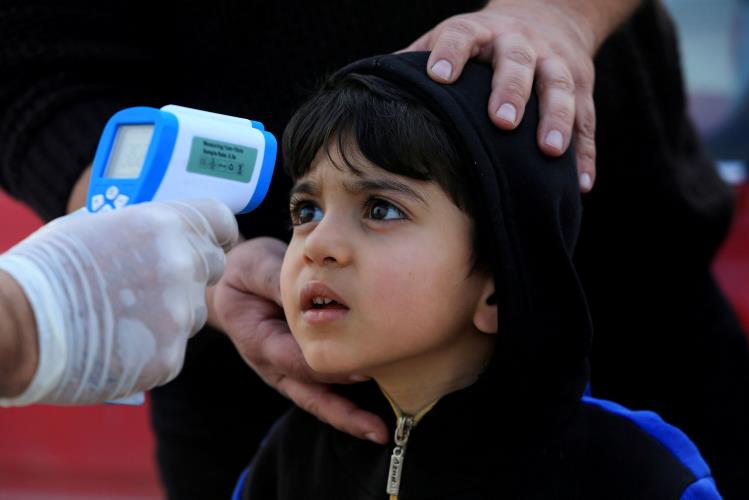 Image: A member of the medical team checks the temperature of a child following the coronavirus outbreak, at a checkpoint on the outskirts of Duhok
