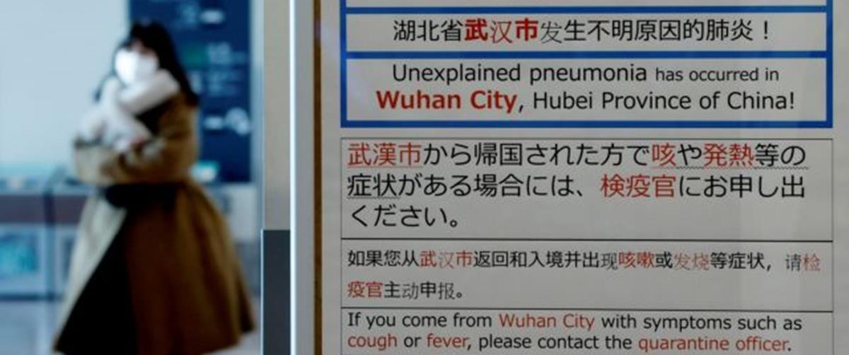 FILE PHOTO: A woman wearing a mask walks past a quarantine notice about the outbreak of coronavirus in Wuhan, China at an arrival hall of Haneda airport in Tokyo